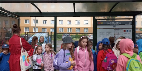 Powiększ grafikę: Grupa dzieci stoi na przystanku autobusowym.
